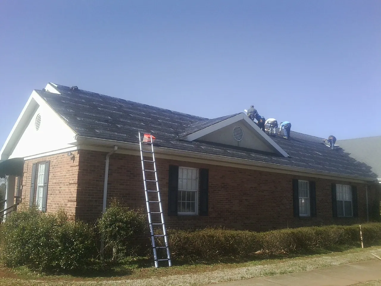 Crew tearing shingles off a brick ranch roof with a ladder set — Metal Roof Repair work by our crew in Mehoopany