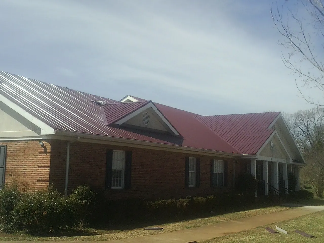 Red metal roof with gabled entries on a long brick building, from a Hail Damage Roof Repair job in Mehoopany