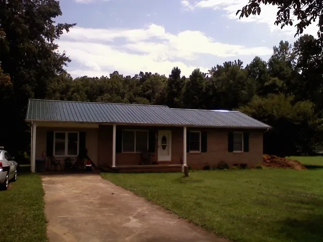 Dark green metal roof on a brick ranch with a covered porch in Mehoopany