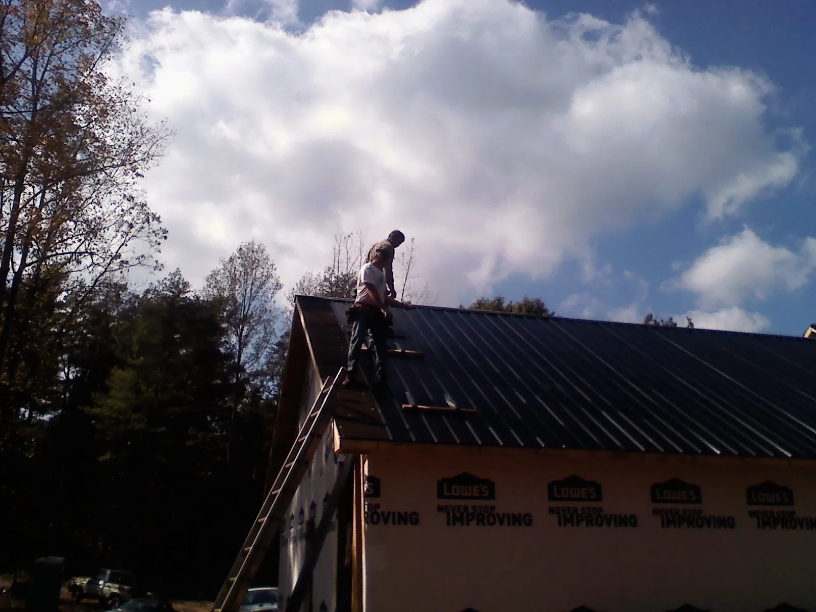 Roofer fastening dark metal panels high against a cloudy sky, from a Roof Inspection job in Mehoopany
