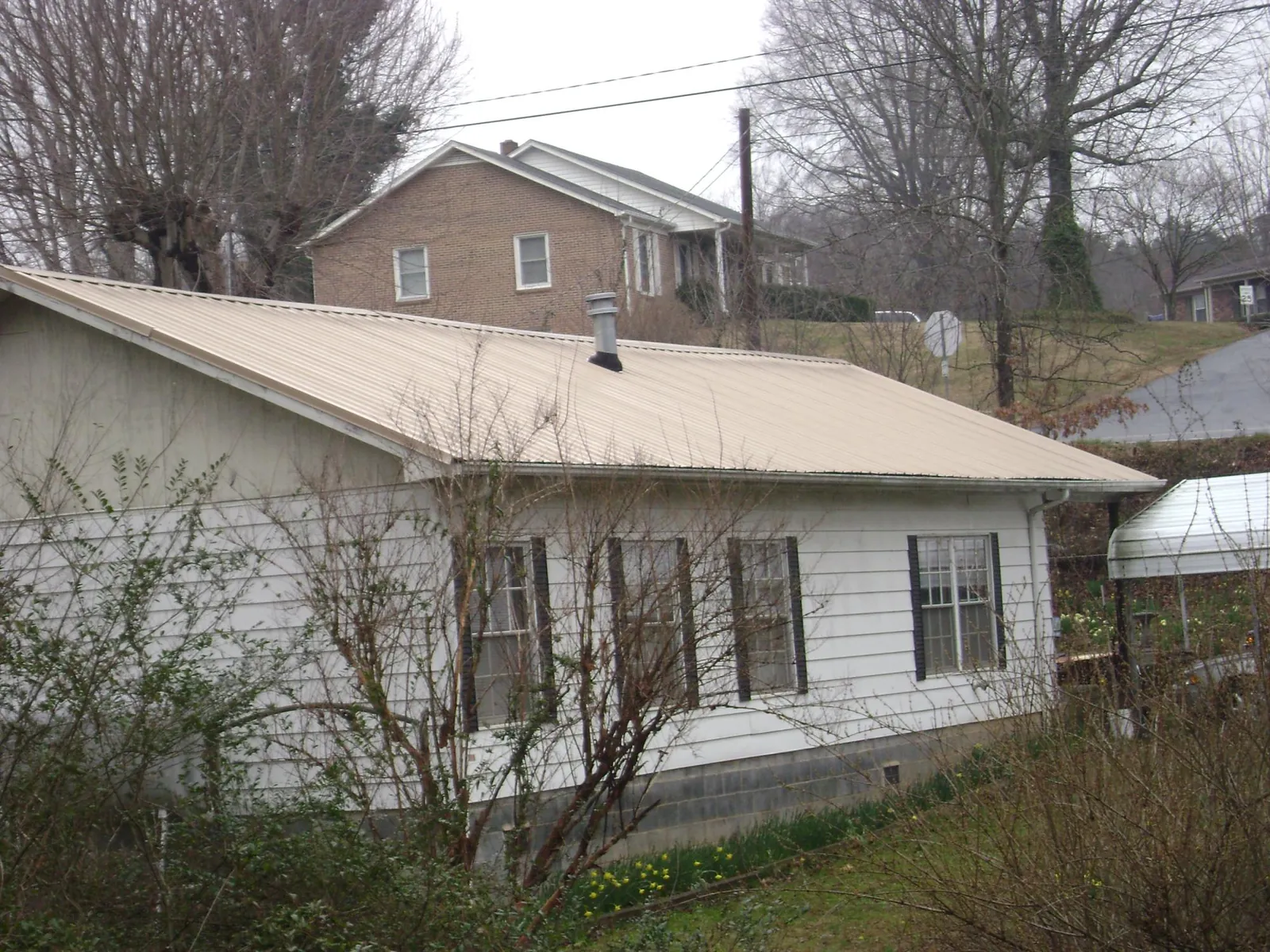Tan metal roof on a white sided house set into a hillside — Commercial Roofing by Roofing Brothers in Mehoopany